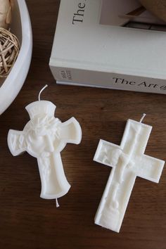 two white candles sitting on top of a wooden table next to a book and vase