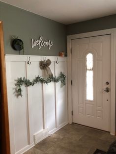 a welcome sign hanging on the wall next to a door with wreaths and greenery