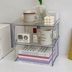 a stack of books and coffee mugs sitting on top of a shelf next to a microwave