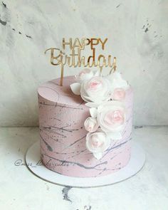 a pink marbled birthday cake with white flowers and a gold happy birthday topper