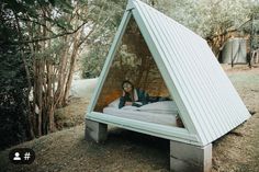 a man laying on top of a bed inside of a triangular shaped structure in the woods