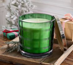 a green glass candle sitting on top of a wooden table next to a christmas tree