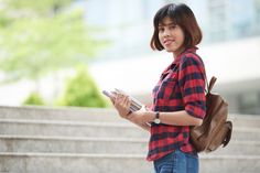 a woman in plaid shirt holding a book and backpack