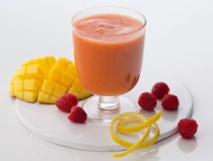 a smoothie with raspberries and mango slices on a white plate next to it