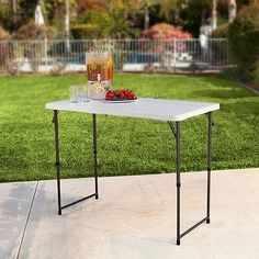 a table with drinks and fruit on it in front of a lawn, next to a swimming pool