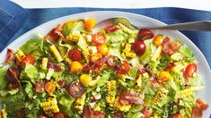 a white plate topped with salad and corn on top of a blue cloth next to a fork