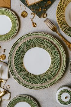 the table is set with green and white plates, silverware, and gold decorations