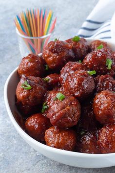 a white bowl filled with meatballs next to a colorful straw and napkin on the table