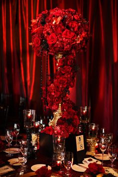 a tall vase filled with red roses on top of a table covered in wine glasses