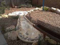 a wooden bench sitting in the middle of a garden next to a stone path that is lined with rocks