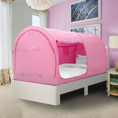 a pink tent bed sitting in a bedroom next to a white table and lamp on top of a rug