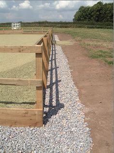 a fenced in area with gravel and rocks on the ground next to an open field