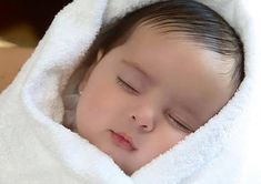 a baby wrapped in a white blanket sleeping on top of a bed with his eyes closed