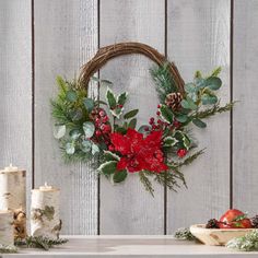 a christmas wreath with red flowers and greenery on a table next to other holiday decorations