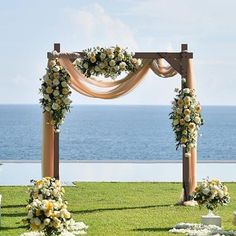 an outdoor wedding setup with flowers and greenery on the grass near the ocean in front of it