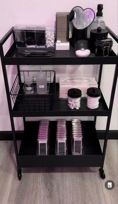 a black shelf filled with lots of items on top of a wooden floor next to a pink wall