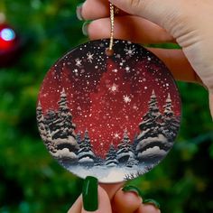 a hand holding up a christmas ornament with trees on it and snowflakes in the background