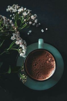 a cup of hot chocolate next to some white flowers on a black background with space for text