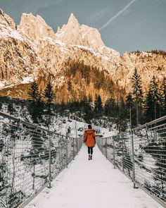 a person walking across a bridge over snow covered ground with mountains in the backgroud