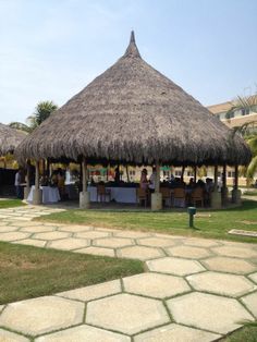 people are sitting at a table under a thatched roof on the grass area in front of some buildings