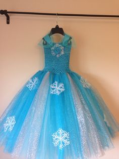 a blue dress with white snowflakes is hanging on a clothes rack in front of a wall