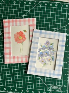 two cards with flowers on them sitting on a cutting board