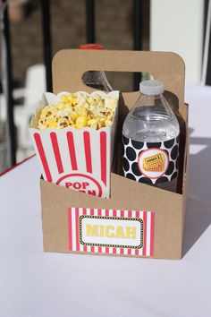 an open box with popcorn and drink on it sitting on top of a white table