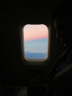 a man sitting in front of a laptop computer on top of a desk next to an airplane window