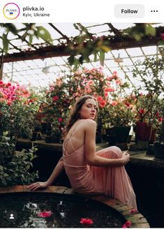 a woman sitting on the ground in front of some flowers and looking up at something