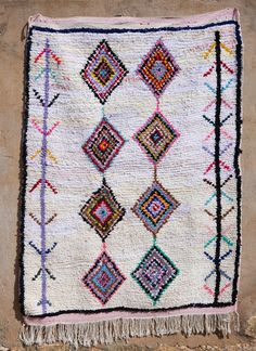 a multicolored rug with fringes hanging on the side of a stone wall