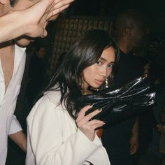 a woman in white jacket holding black purse next to other people at table with food and drinks