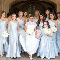 a group of women standing next to each other in front of a building holding bouquets