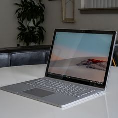 an open laptop computer sitting on top of a white table next to a potted plant