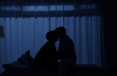 two people are kissing in the dark with curtains on the window sill behind them