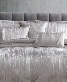 a bed with silver sheets and pillows on it's headboard, in front of a gray wall