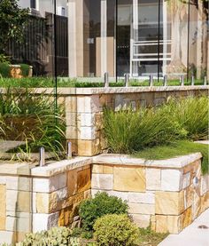 there is a bench made out of stone blocks and plants in front of the building