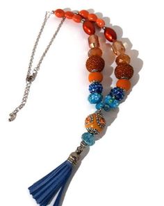 ANDREA DESIGNS STATEMENT NECKLACE WITH BLUE LEATHER TASSEL, THE ORANGE PEACOCK NECKLACE, BOHO CHIC STYLE This necklace will add pizzazz to any outfit. The necklace was made with a metal chain and beads. The beads were strung using a bead stringing wire (nylon coated stainless steel), the color of the beads are orange and blue, (orange and blue metal lining beads, blue glass beads, and metal beads), the pendant is formed by an orange metal lining beaded bead, blue glass beads, and a blue leather Turquoise Necklaces With Tassel And Round Beads, Turquoise Necklace With Tassels And Round Beads, Orange Beaded Dangle Necklaces, Orange Bohemian Beaded Necklace With Dangling Beads, Orange Bohemian Beaded Necklaces With Dangling Beads, Colorful Beaded Bohemian Jewelry, Bohemian Colorful Beaded Jewelry, Bohemian Orange Beaded Necklaces For Jewelry Making, Orange Bohemian Beaded Necklaces For Jewelry Making