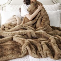 a woman laying on top of a bed under a blanket covered in brown furs