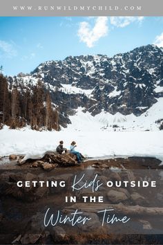 two people sitting on rocks in the snow with mountains behind them and text overlaying reading getting kids outside in the winter time