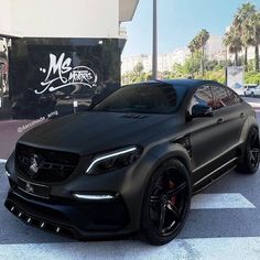 a black mercedes suv is parked in front of a car dealership with palm trees behind it