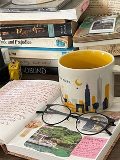 a coffee cup sitting on top of an open book next to some books and glasses