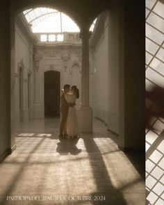 two people are standing in the middle of a hallway with sunlight coming through the windows