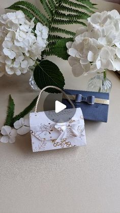 a vase with white flowers and a blue gift bag on it next to a bouquet of hydrangeas