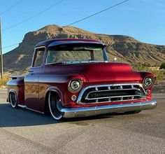 an old red truck is parked on the side of the road in front of mountains