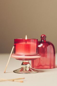 a red candle sitting on top of a table next to a glass container with matches