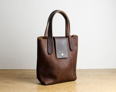 a brown leather bag sitting on top of a wooden table next to a white wall