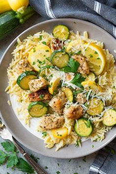 a white plate topped with pasta covered in meat and veggies next to zucchini