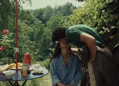 two people are kissing under an umbrella near a table with food and drinks on it