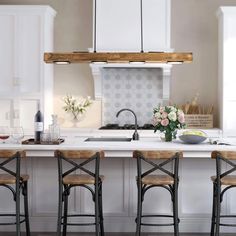 a kitchen island with four stools in front of it and flowers on the counter