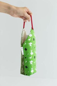 a hand holding a green bag with white and black flowers on it, hanging from a red string